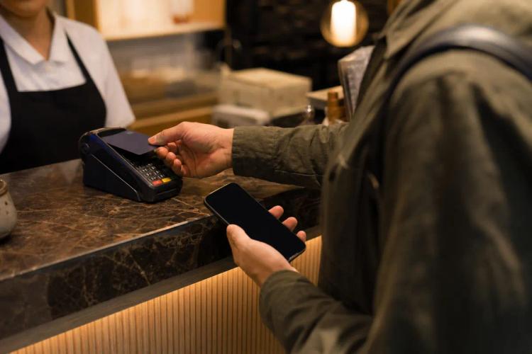Client payant sans contact avec sa carte sur un terminal, smartphone dans l'autre main au comptoir