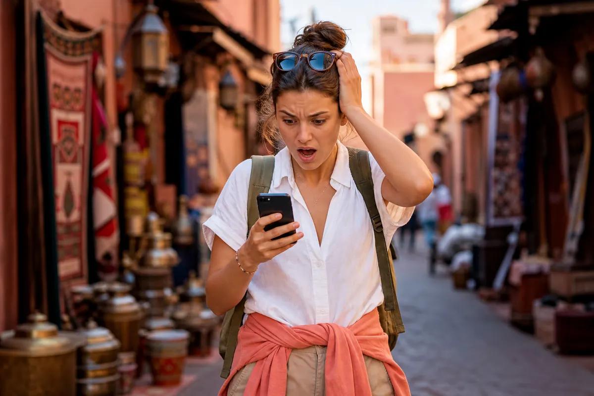 Voyageuse choquée devant son smartphone dans une ruelle de souk bordée de tapis et de lanternes