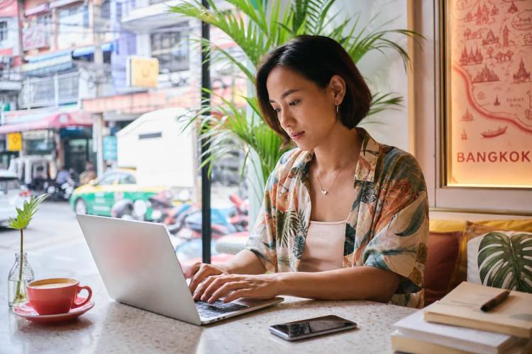 Femme travaillant sur son ordinateur portable dans un café de Bangkok, smartphone posé sur la table