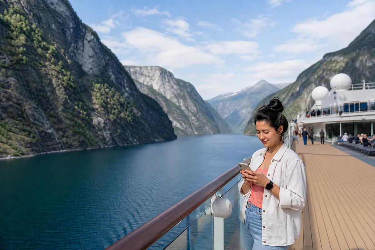 Passagère consultant son téléphone au bastingage d'un navire naviguant dans un fjord norvégien