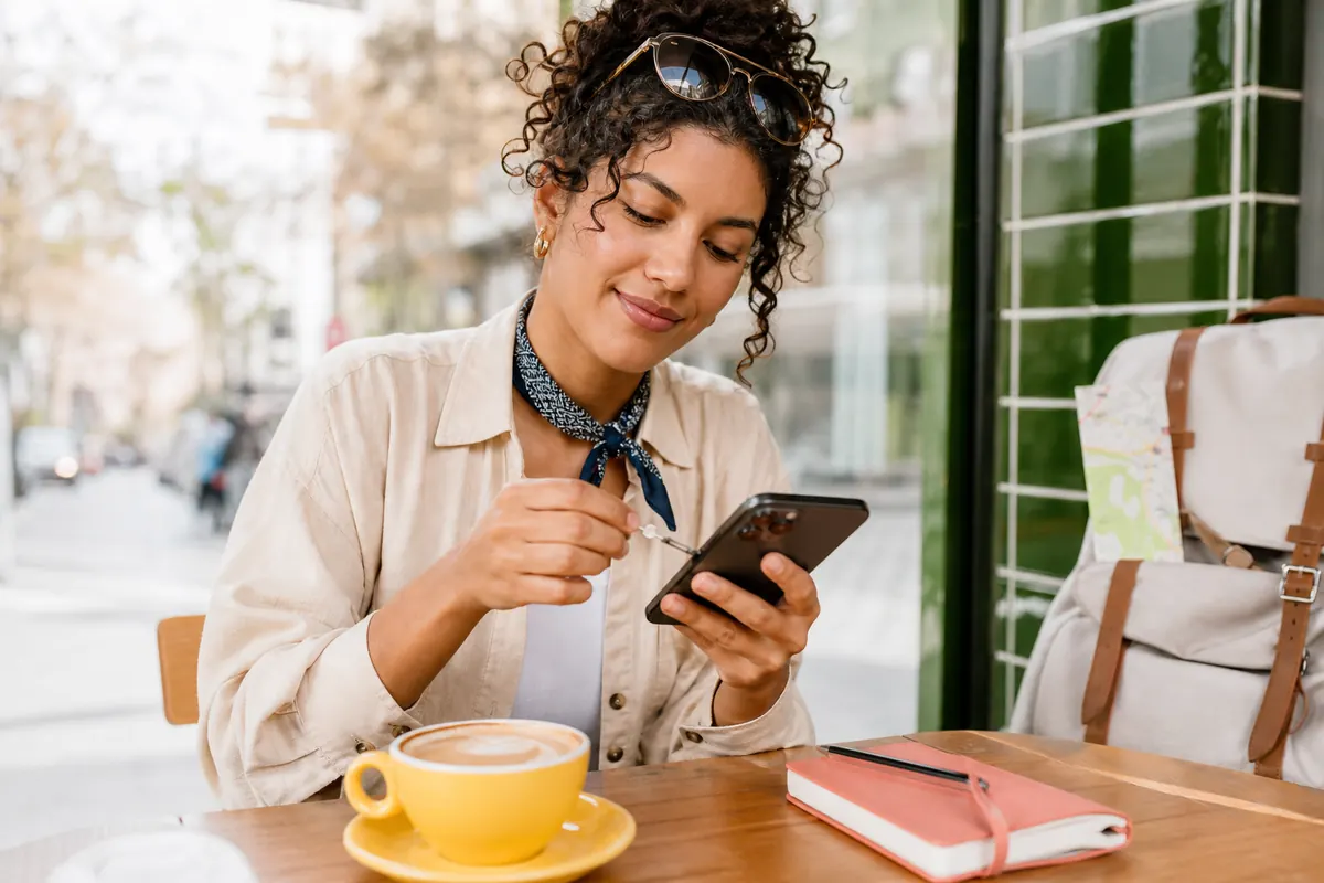 Traveler opening the SIM tray of their smartphone with a paperclip at an airport cafe.