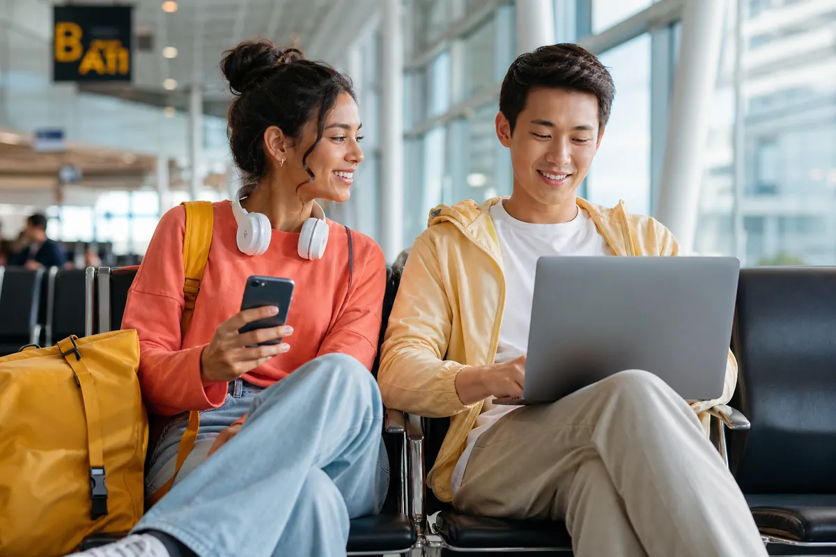 Voyageurs partageant une connexion hotspot sur ordinateur dans un terminal d'aéroport.