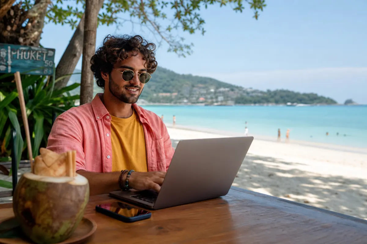 Voyageur travaillant sur ordinateur via hotspot mobile sur une plage de Phuket.