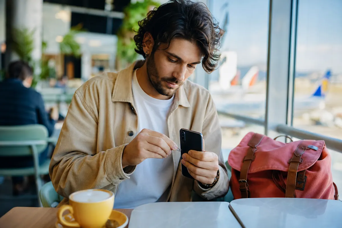 Voyageur retirant sa carte SIM physique de son smartphone à l'aéroport.